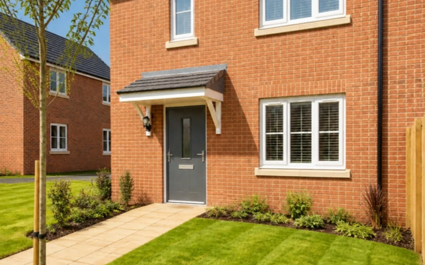 New-build red brick house with a freshly turfed front lawn, a young tree and a paved path to the door